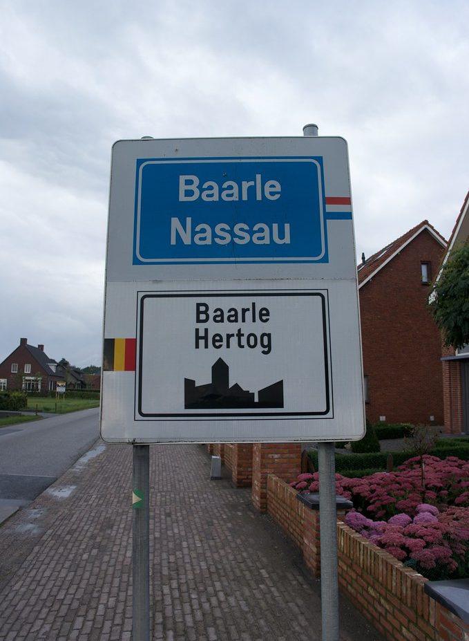Signpost indicating the border between Baarle Nassau and Baarle Hertog, featuring town names and local flags.
